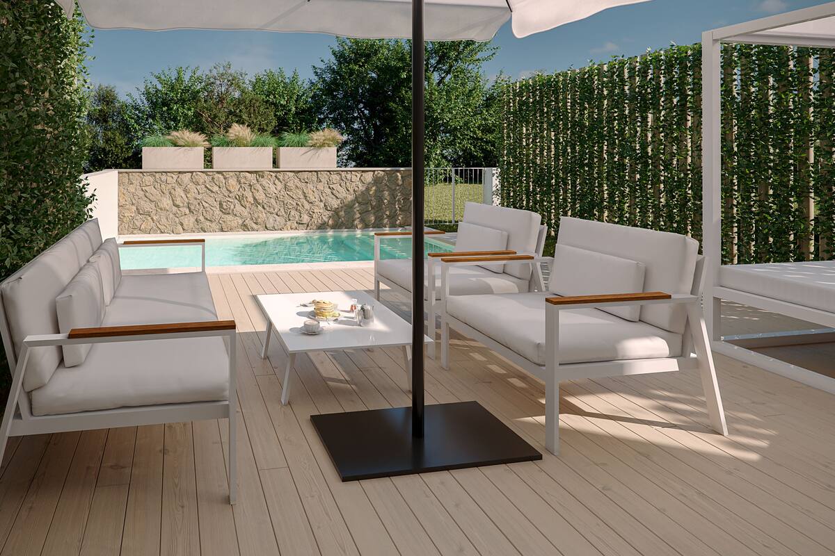 A modern outdoor seating area with white sofas and a table, overlooking a swimming pool and lush greenery.
