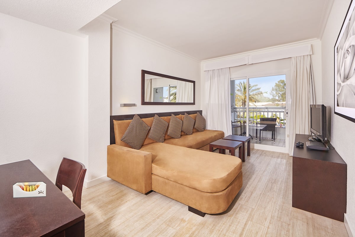 A modern living room with a sofa, a dining table, a TV, and a balcony with a view.