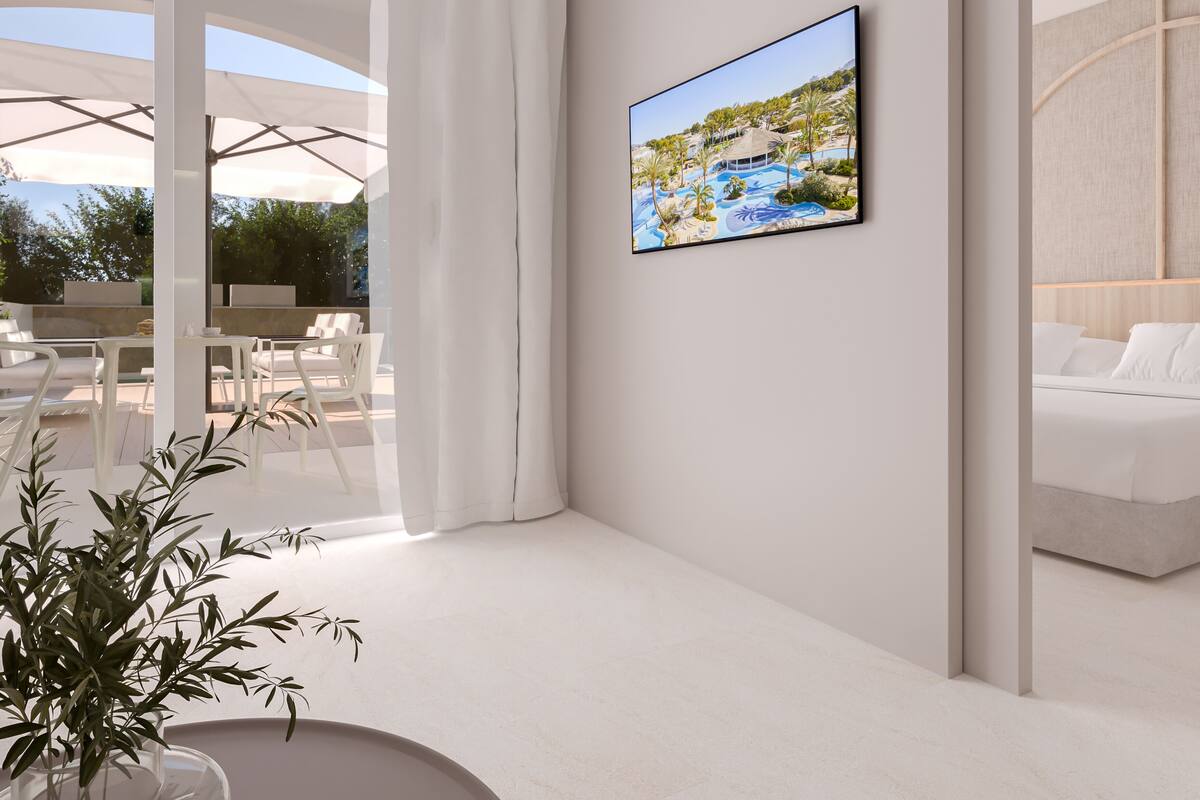 A modern hotel room with a large window, a bed, a dining area with white furniture, and a framed picture on the wall.