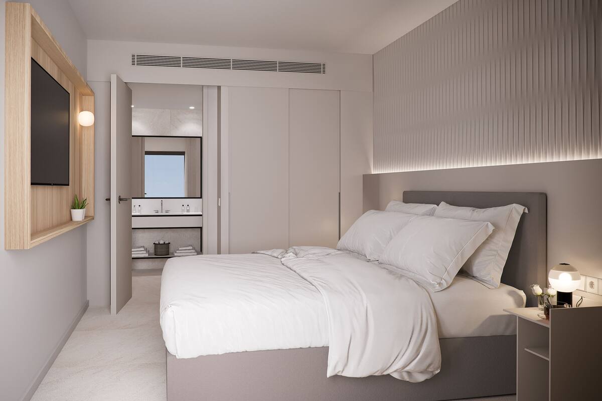 A modern bedroom with a large bed, a bedside table, a built-in wardrobe, and a mirror above the mirror cabinet.