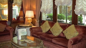 Ein komfortables, rotes Sofa mit drei Kissen, ein Glastisch mit einem Buch mit dem Titel „Curiosando Venezia“ und eine Lampe auf einem Beistelltisch.