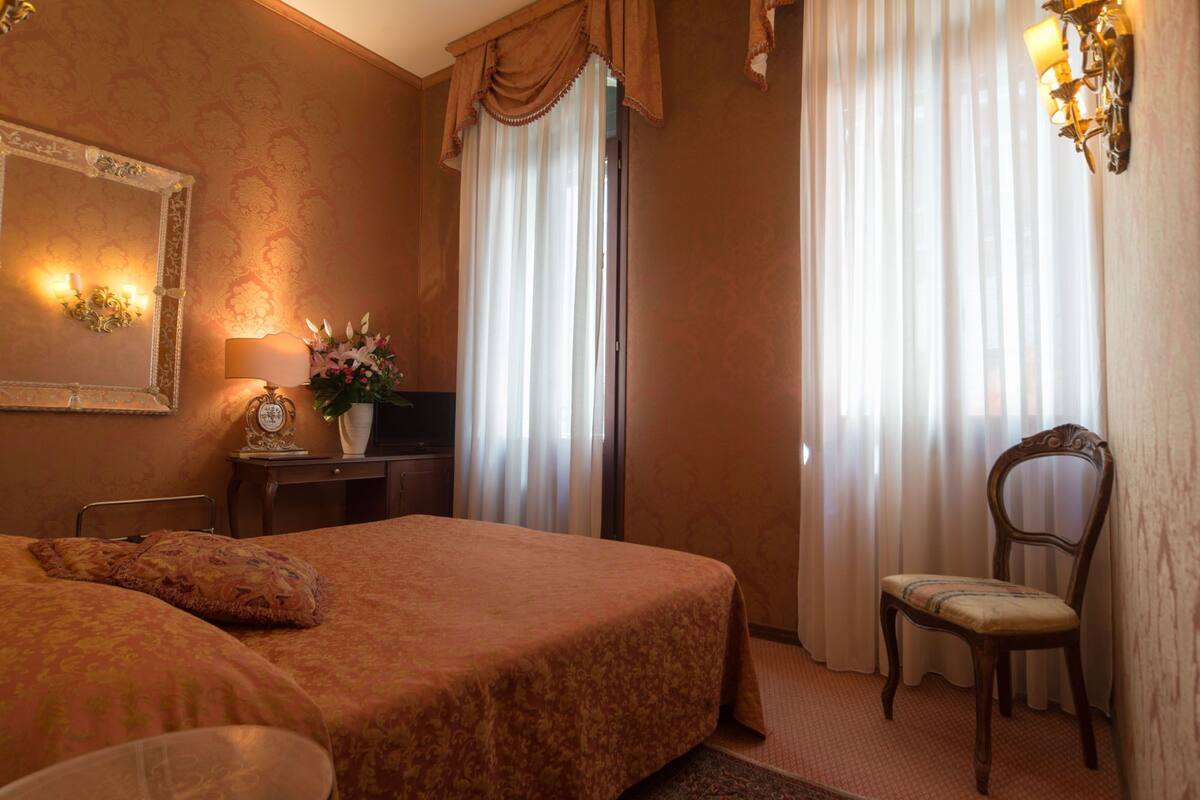 Une chambre d’hôtel avec un grand lit, un bureau avec une lampe, une chaise et un téléviseur.