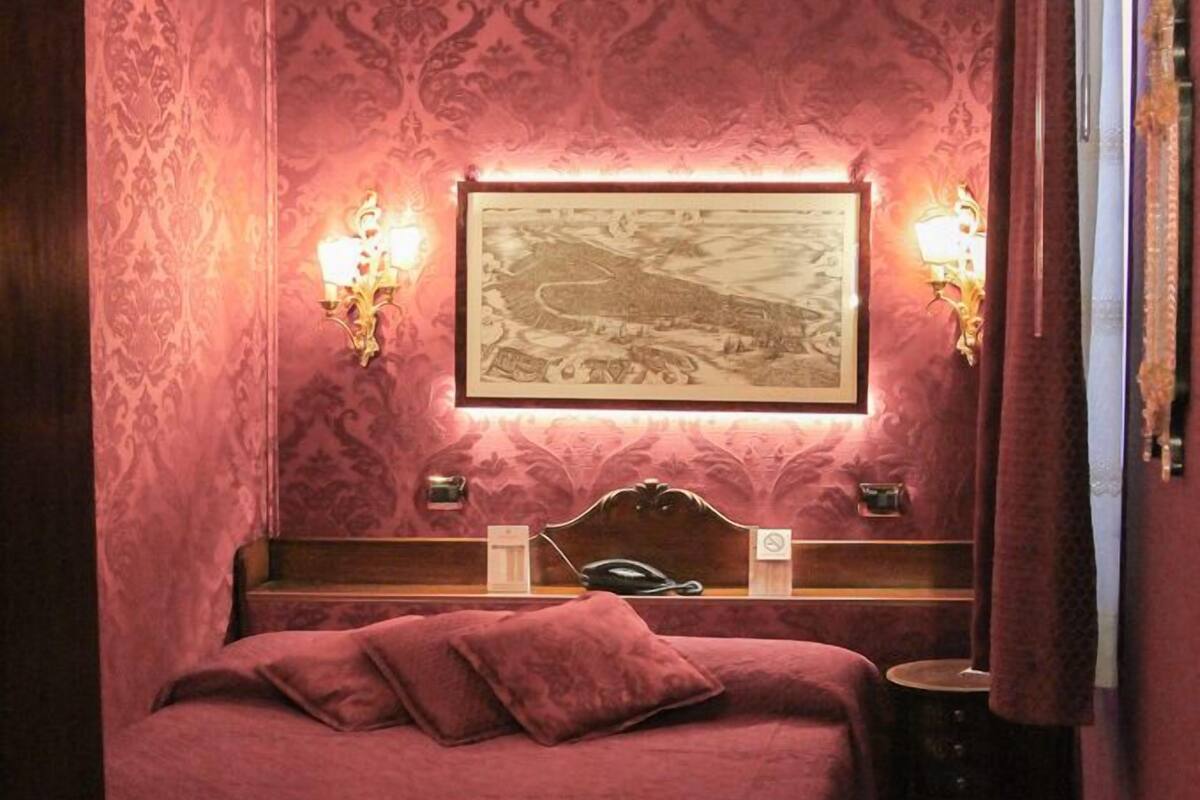 Une chambre d’hôtel avec un grand lit, deux lampes de chevet, un tableau encadré au mur et une table de chevet avec une télécommande.