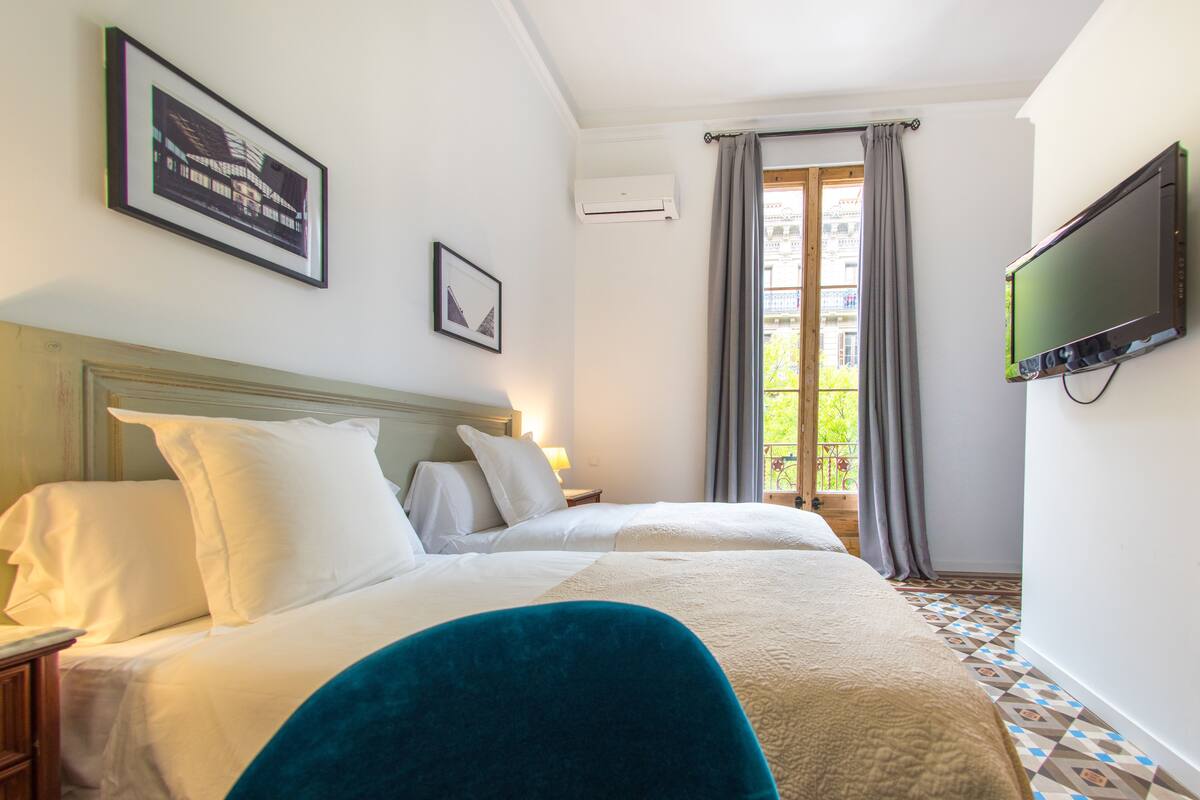 A hotel room with a large bed, a television, a window with curtains, and a framed picture on the wall.