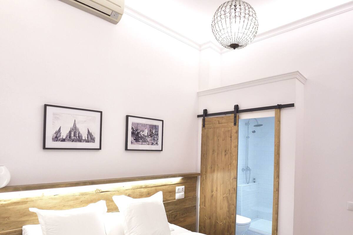 A bedroom with a large bed, a wooden headboard, a ceiling light, and a sliding door leading to a bathroom.