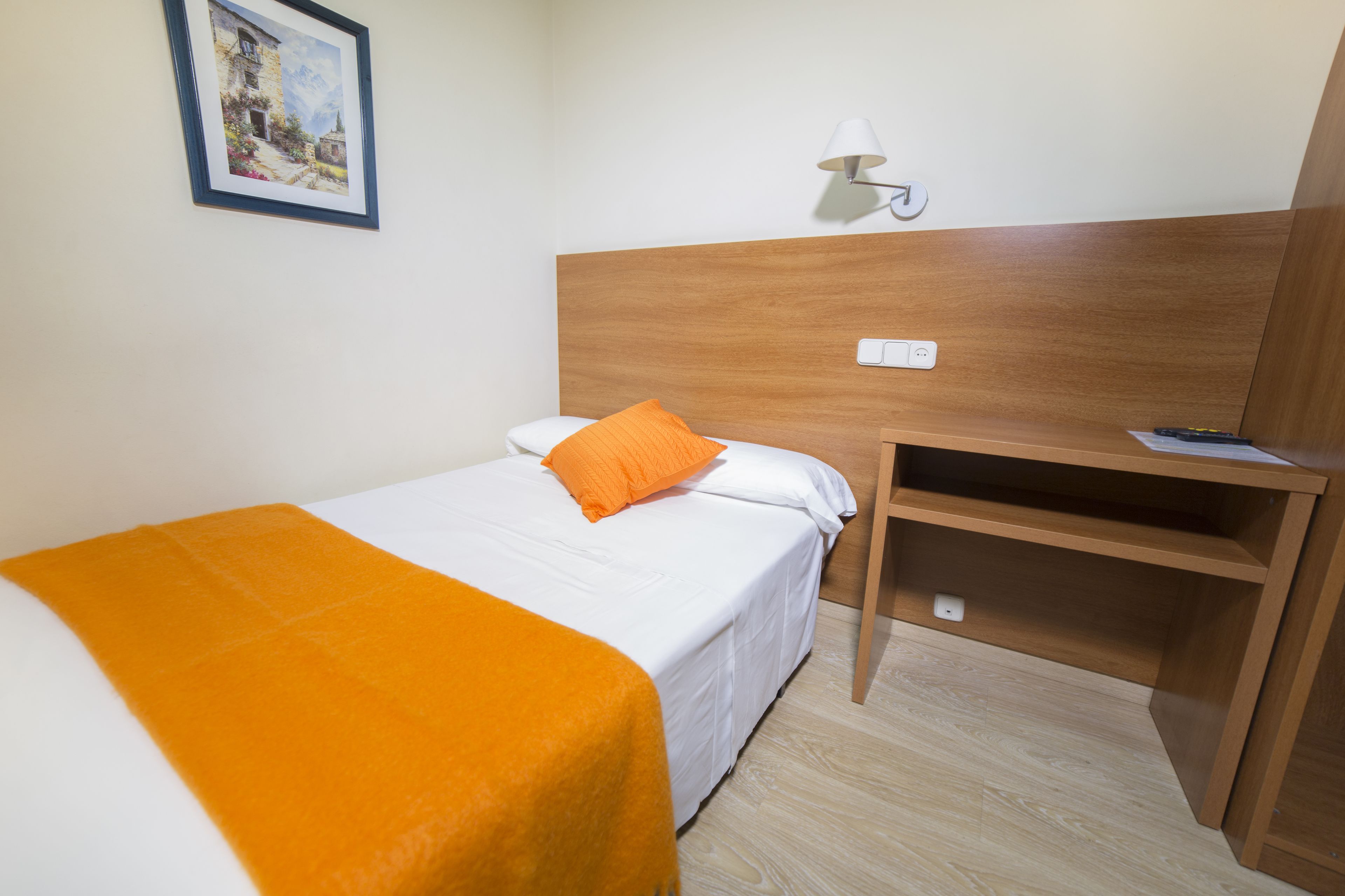 Una habitación de hotel con una cama, un escritorio, una lámpara y un cuadro en la pared.