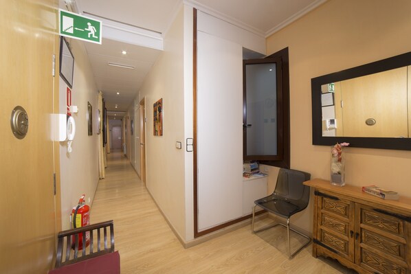 Un pasillo de hotel con un banco de madera, un extintor, un espejo y una puerta con letrero de salida de emergencia.