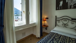 A hotel room with a bed, a window with curtains, a lamp, and a wall-mounted picture. - In Riva al Lago (Como)
