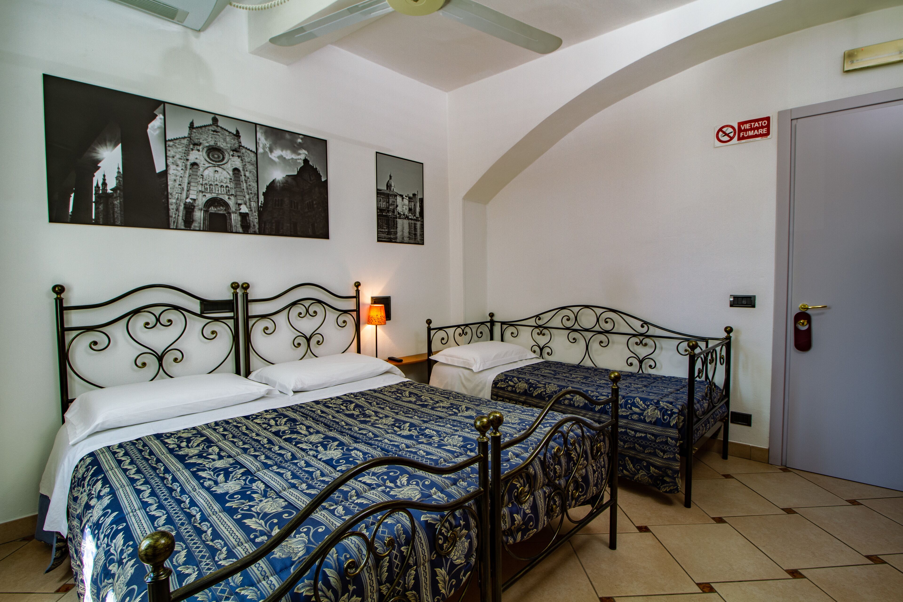 Una stanza con due letti, un'opera d'arte appesa al muro, una porta con un cartello e una ventola a soffitto.