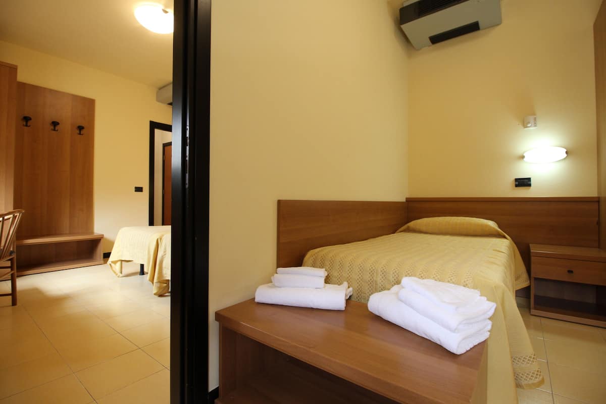 A hotel room with a bed, a wooden nightstand, a chair, and a bench.