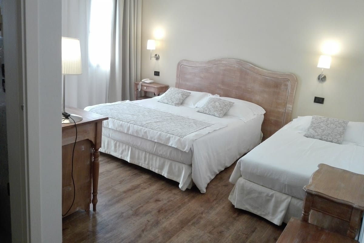 Habitación de hotel con una cama grande, dos mesitas de noche, un escritorio con lámpara y una ventana con cortinas.