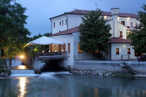 A riverside building with a bridge, a waterfall, and a white umbrella. - Antico Mulino (Scorze)