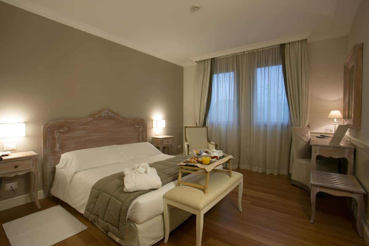 Habitación de hotel con una cama grande, mesitas de noche con lámparas, un escritorio con una silla y una ventana con cortinas.
