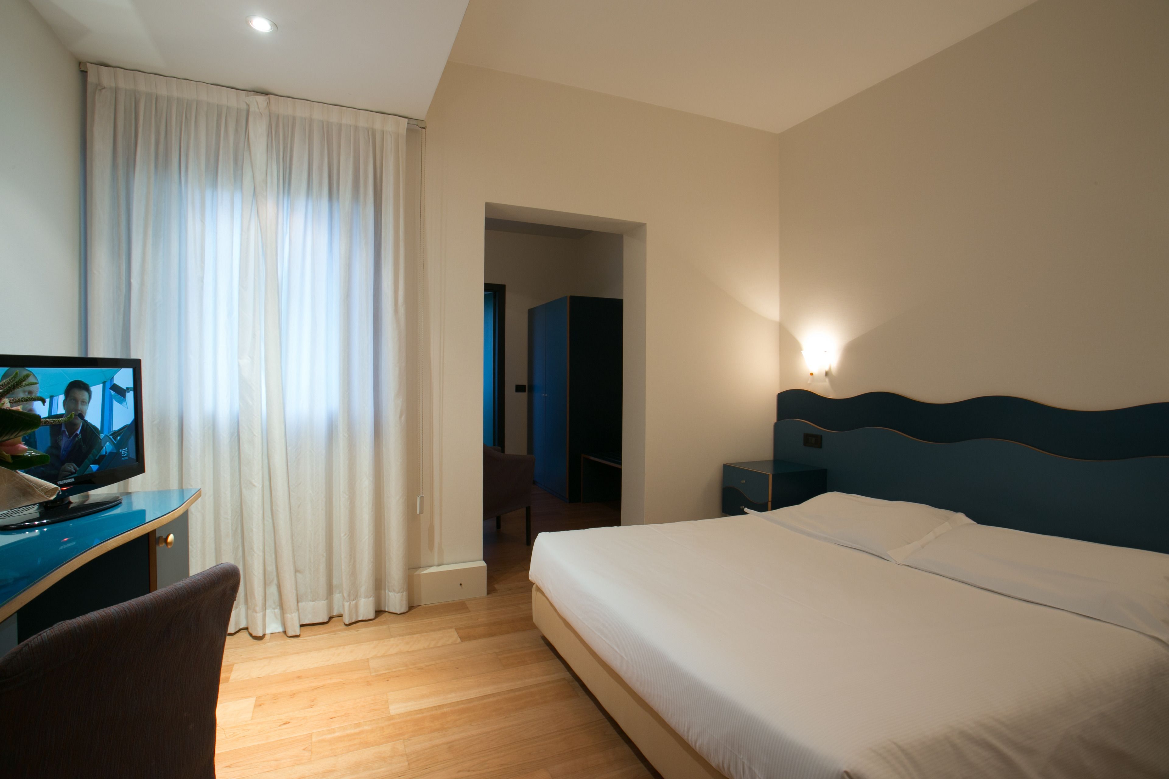 A hotel room with a bed, a desk with a computer, a chair, and a wardrobe.