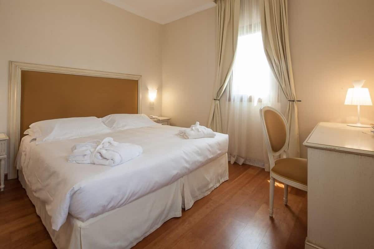 Una habitación de hotel con una cama grande, una silla, un escritorio y una lámpara.