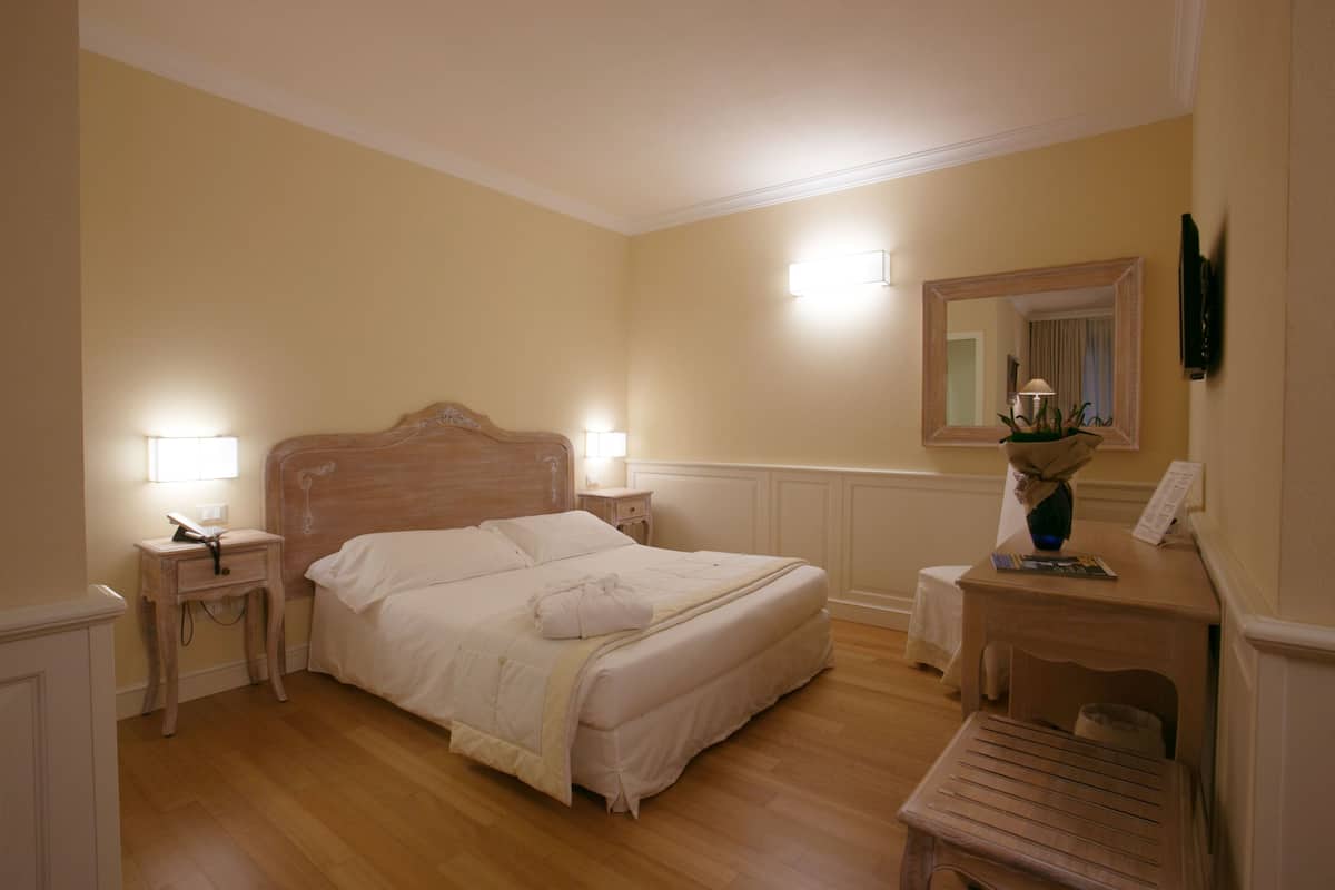 Un dormitorio ordenado con cama, mesitas de noche, una silla y un espejo.