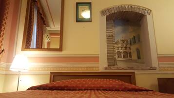 A hotel room with a bed, a mirror, a framed picture of a building, and a lamp.