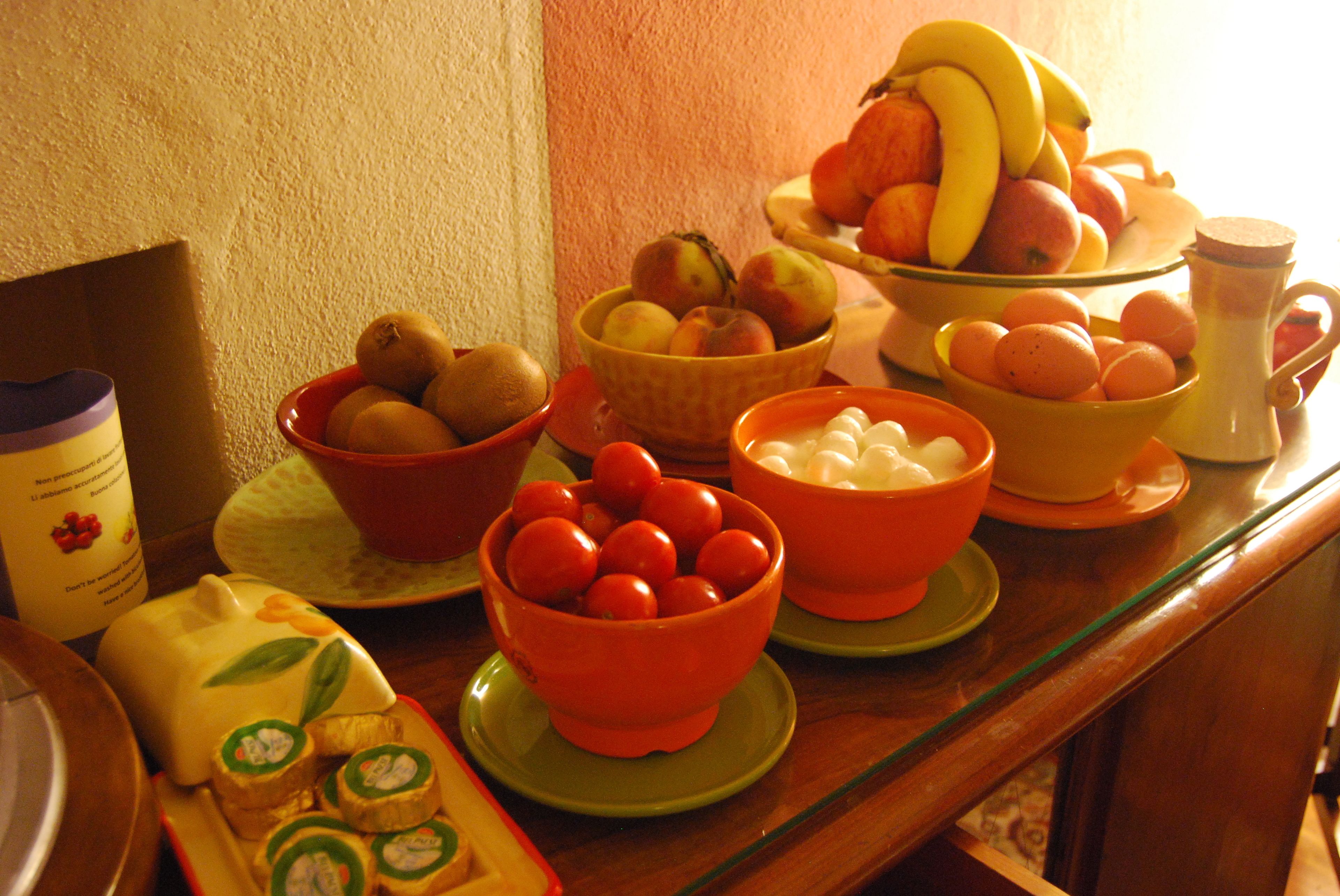 A table with various bowls containing fruits and vegetables, a pitcher, and a packet of snacks.