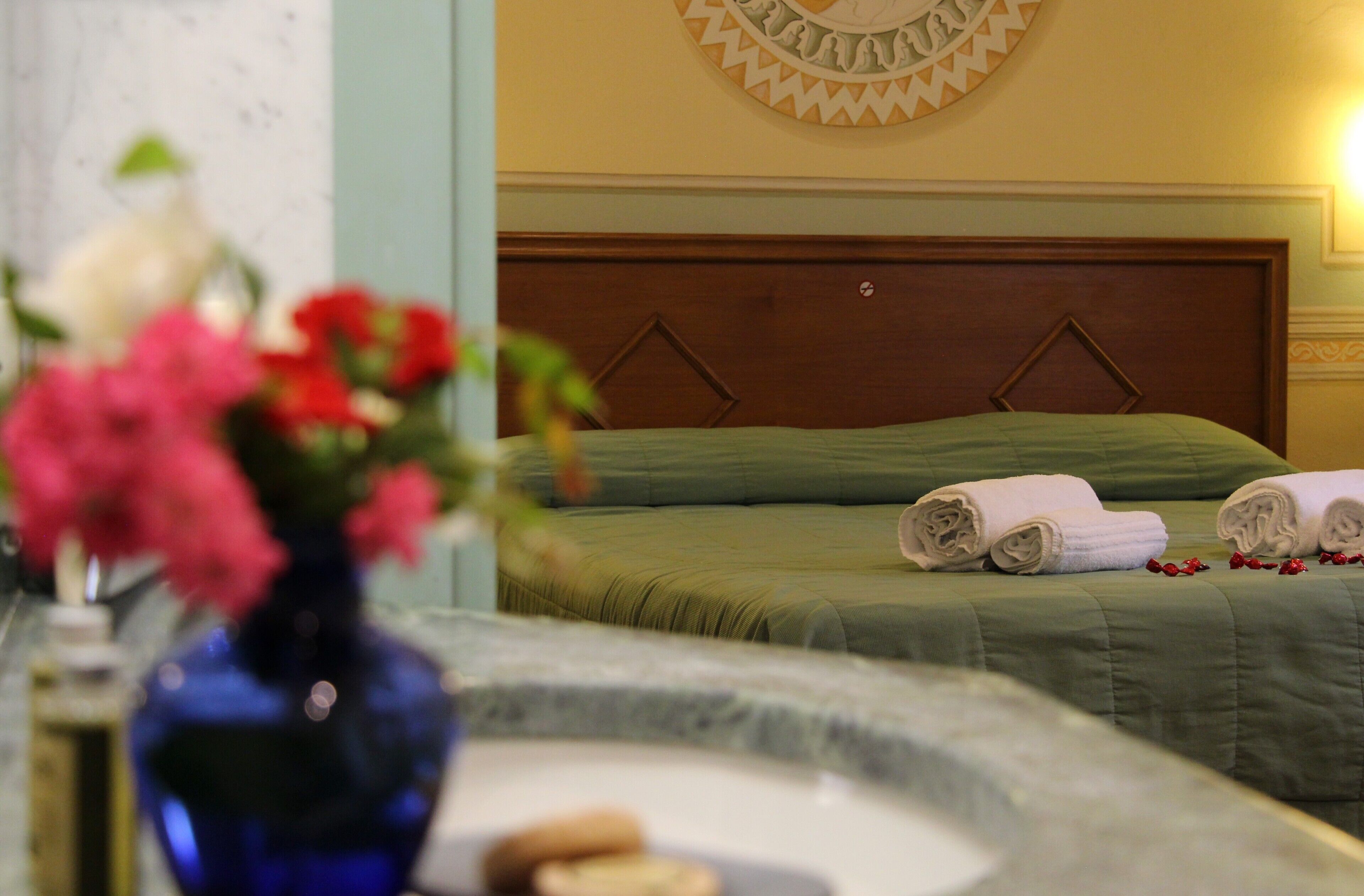 A hotel room with a bed, a nightstand, and a vase with flowers.