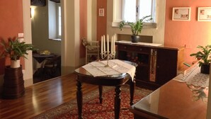 Un comedor con una mesa de madera, sillas, una lámpara de araña y un ventanal con una planta en el alféizar.