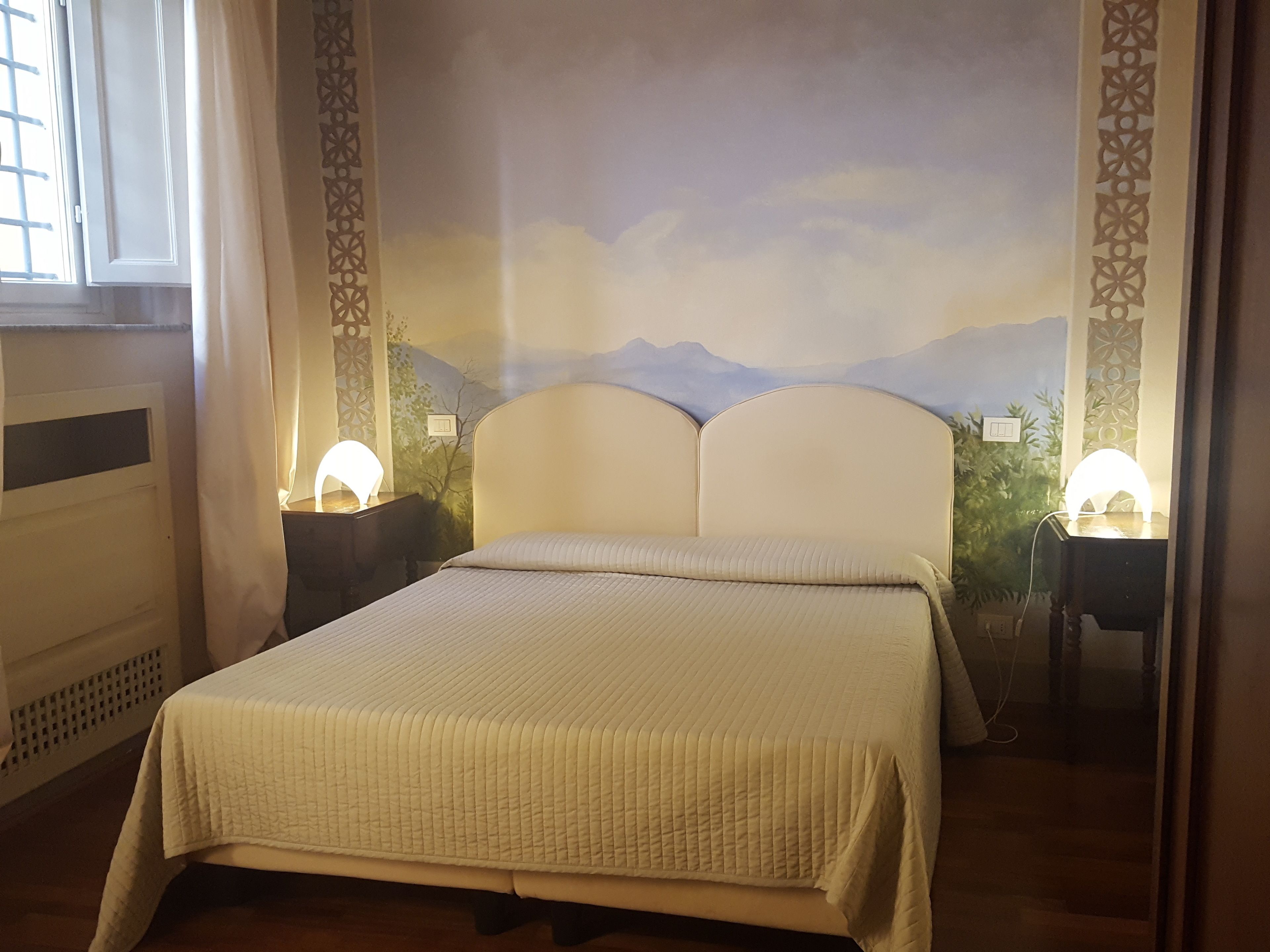A bedroom with a bed, two bedside lamps, a window, and a decorative wall mural.