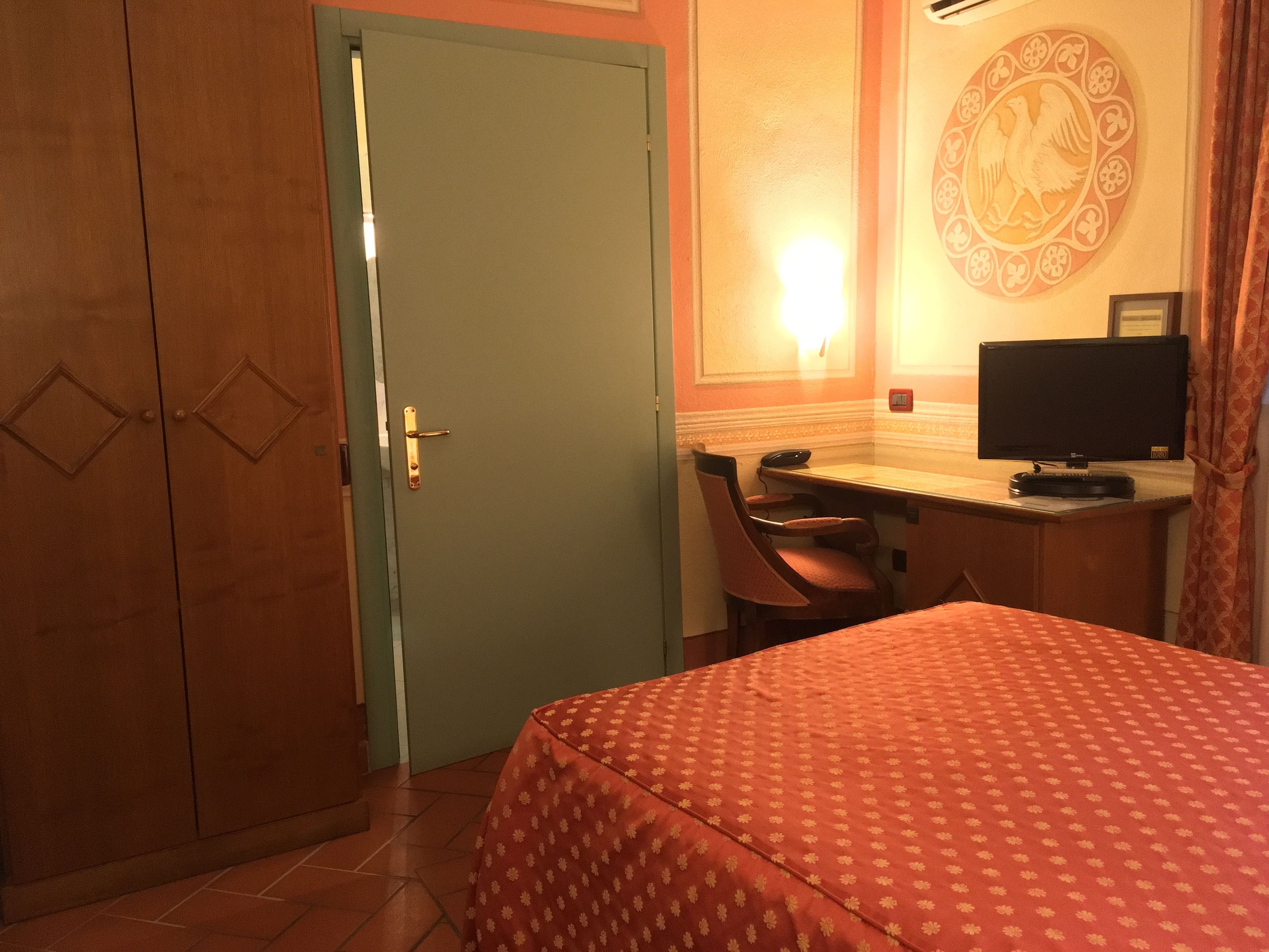 Ein Hotelzimmer mit Bett, Schreibtisch, Computer, Stuhl und Kleiderschrank.