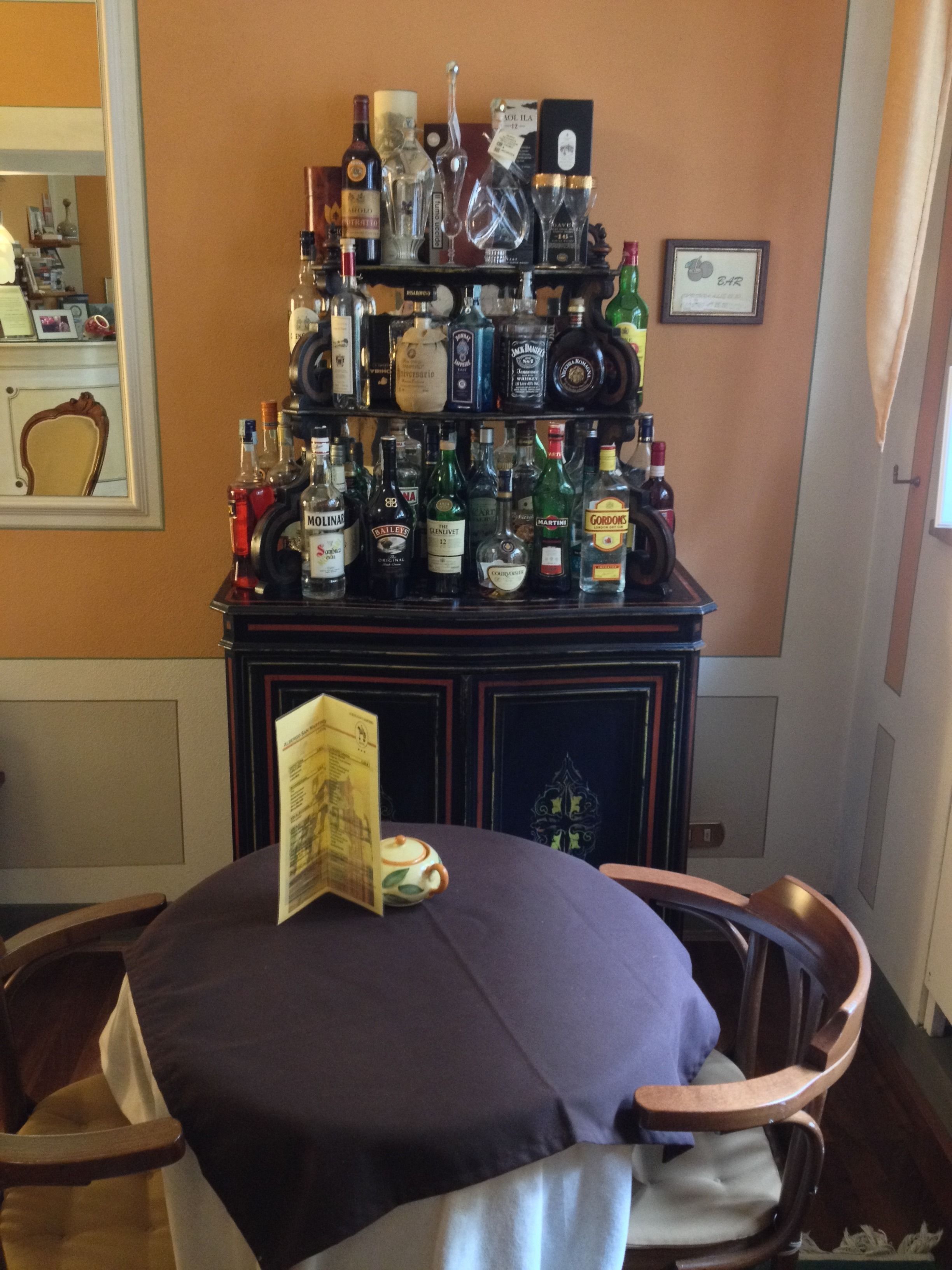 Un coin bar avec un assortiment de bouteilles et de verres, un menu posé sur la table et un certificat encadré accroché au mur.