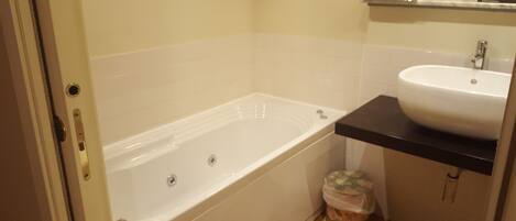 A bathroom with a bathtub, a sink, and a trash bin.