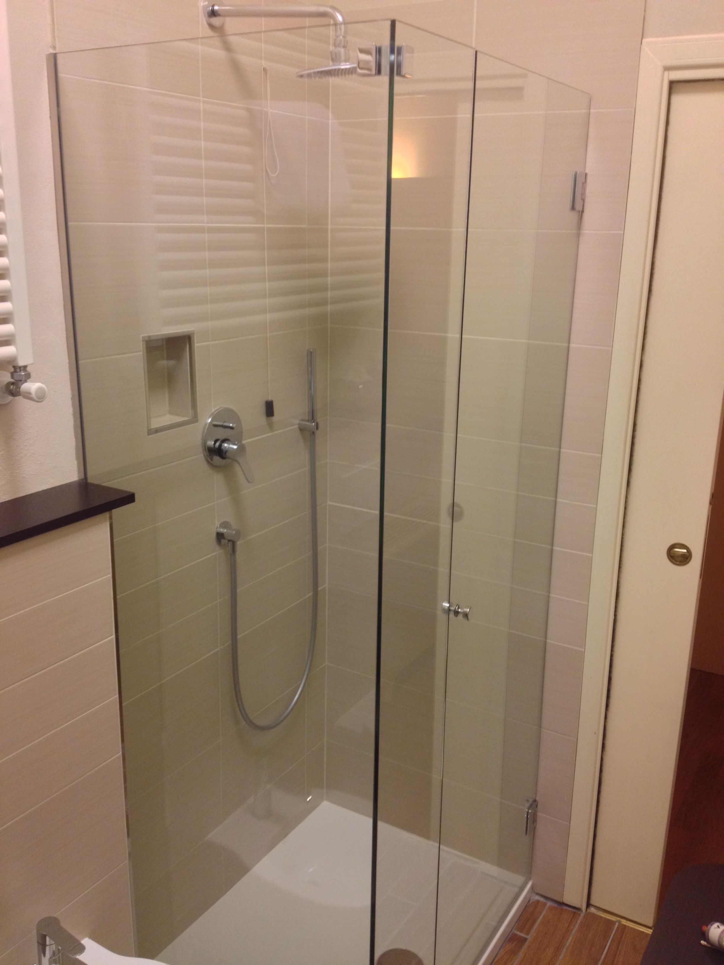 A glass-enclosed shower stall with a handheld showerhead and a wall-mounted faucet.