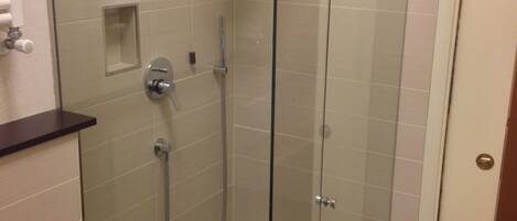 A glass-enclosed shower stall with a handheld showerhead and a wall-mounted faucet.