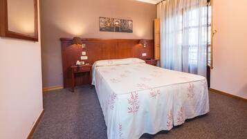 A hotel room with a bed, a nightstand, a lamp, a painting on the wall, and a window with curtains.