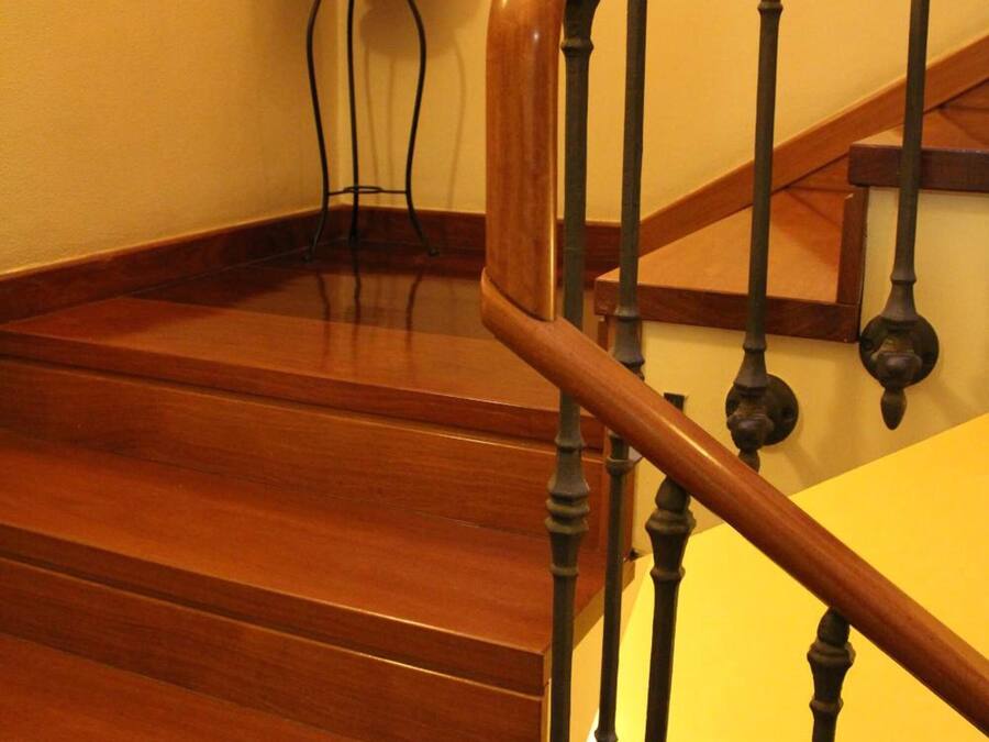 Una escalera de madera con barandilla y una mesita con un arreglo floral a su lado.