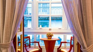 Una habitación con una mesa y dos sillas, una ventana que da a un edificio y un balcón con barandilla.