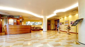 A hotel lobby with a reception desk, a clock, a large abstract painting, and a check-in counter. - Primhotel (Oderzo)