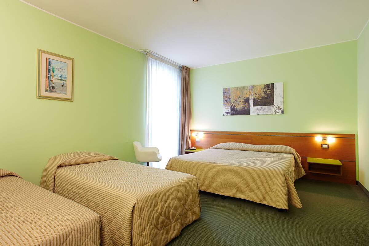 Quarto de hotel com duas camas, uma cadeira e obras de arte na parede.