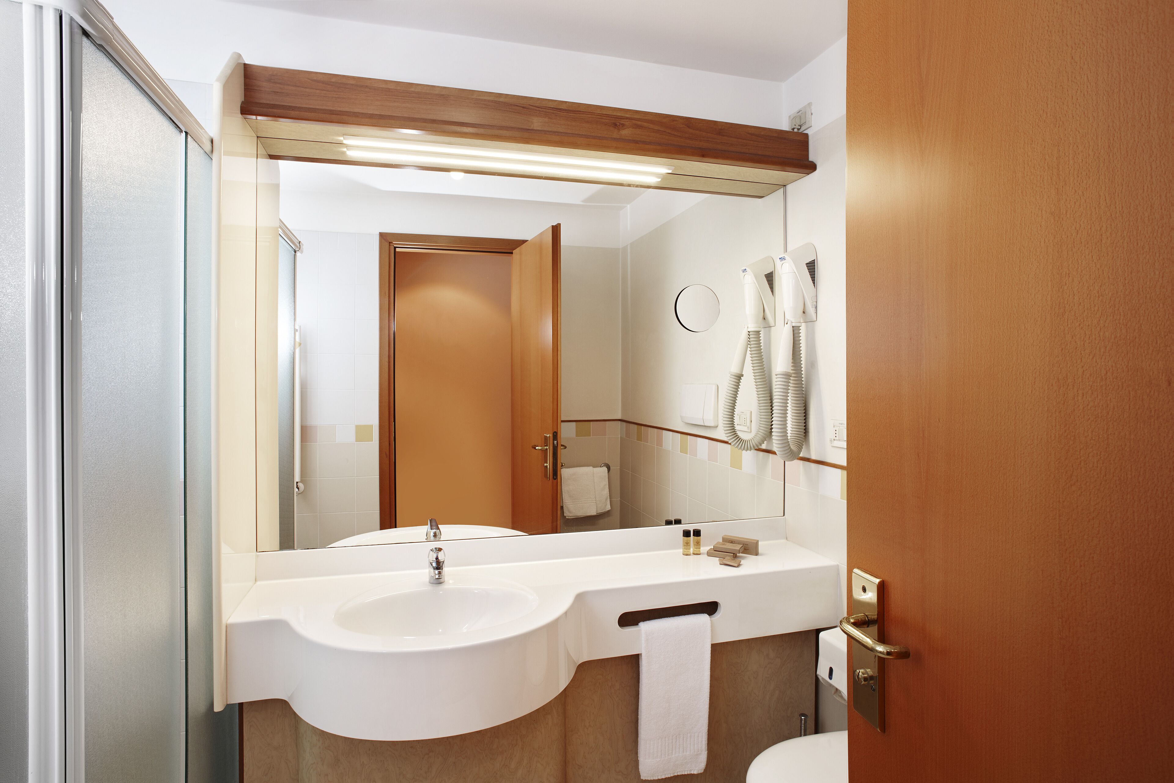 Une salle de bain moderne avec un grand miroir, deux lavabos et un sèche-cheveux fixé au mur.