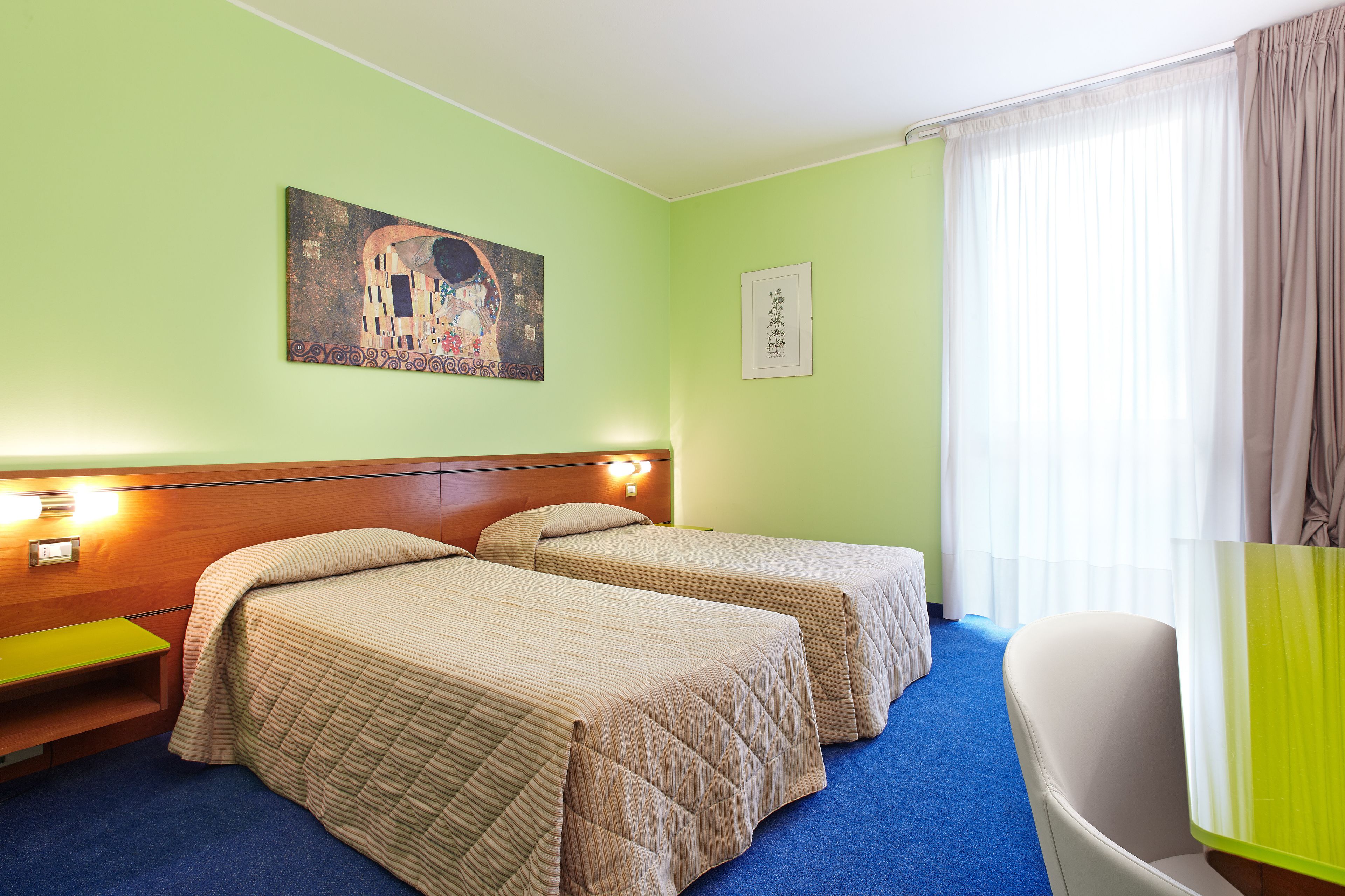 A hotel room with two beds, a bench, a chair, and artwork on the walls.