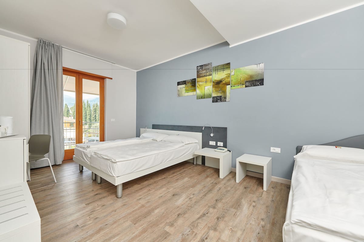 A modern hotel room with a large bed, a desk, a chair, and a view of the outdoors.