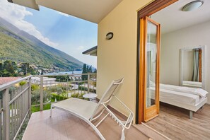 A balcony with a lounge chair, a small table, and a bed with a wooden frame. - Eco Hotel Benacus (Malcesine)