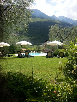 A poolside area with lounge chairs and umbrellas, surrounded by lush greenery and mountains in the background. - Eco Hotel Benacus (Malcesine)