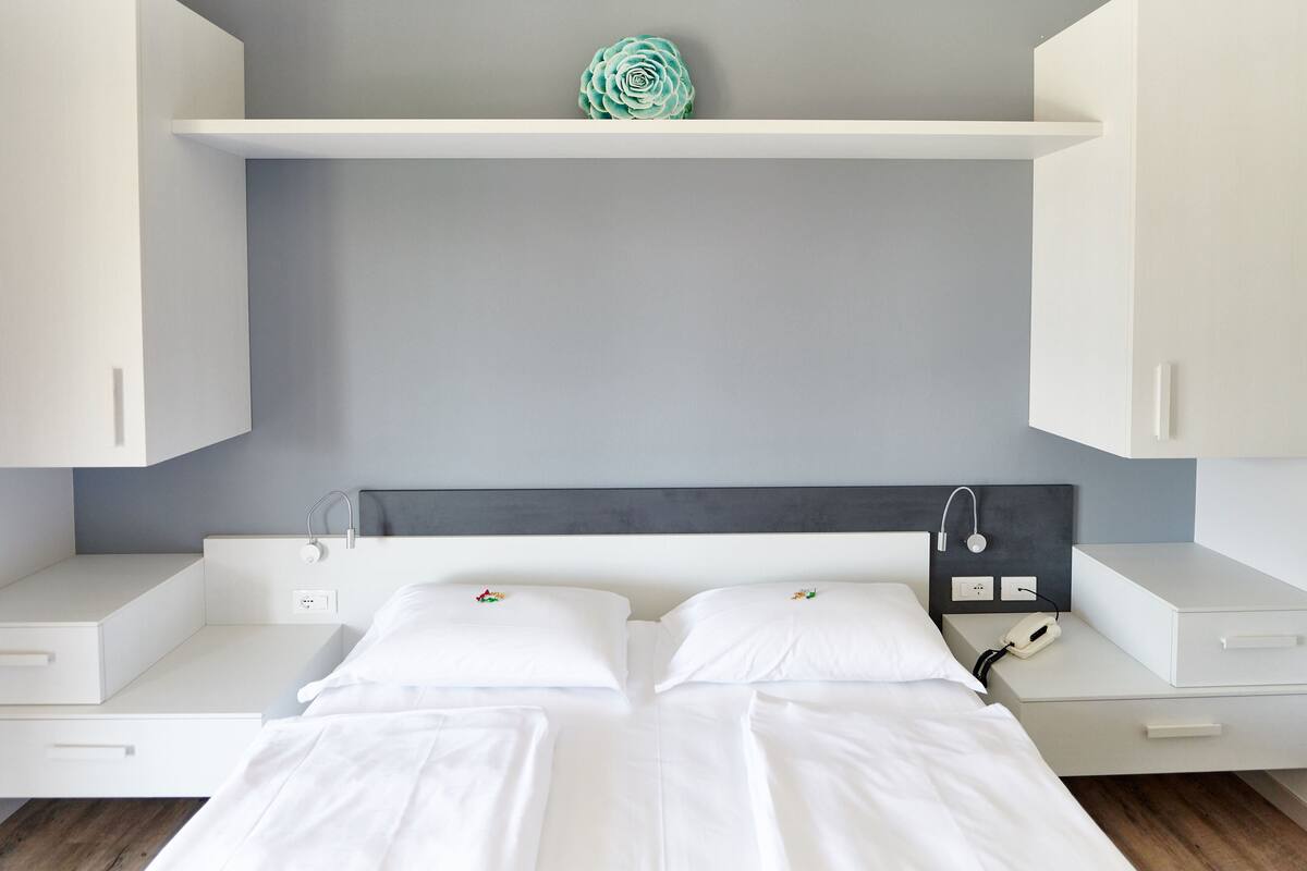 A modern bedroom with a bed, white cabinets, a gray wall, and a decorative item on the shelf.