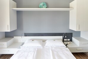 A modern bedroom with a bed, white cabinets, a gray wall, and a decorative item on the shelf. - Eco Hotel Benacus (Malcesine)