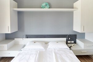 A modern bedroom with a bed, white cabinets, a gray wall, and a decorative item on the shelf.