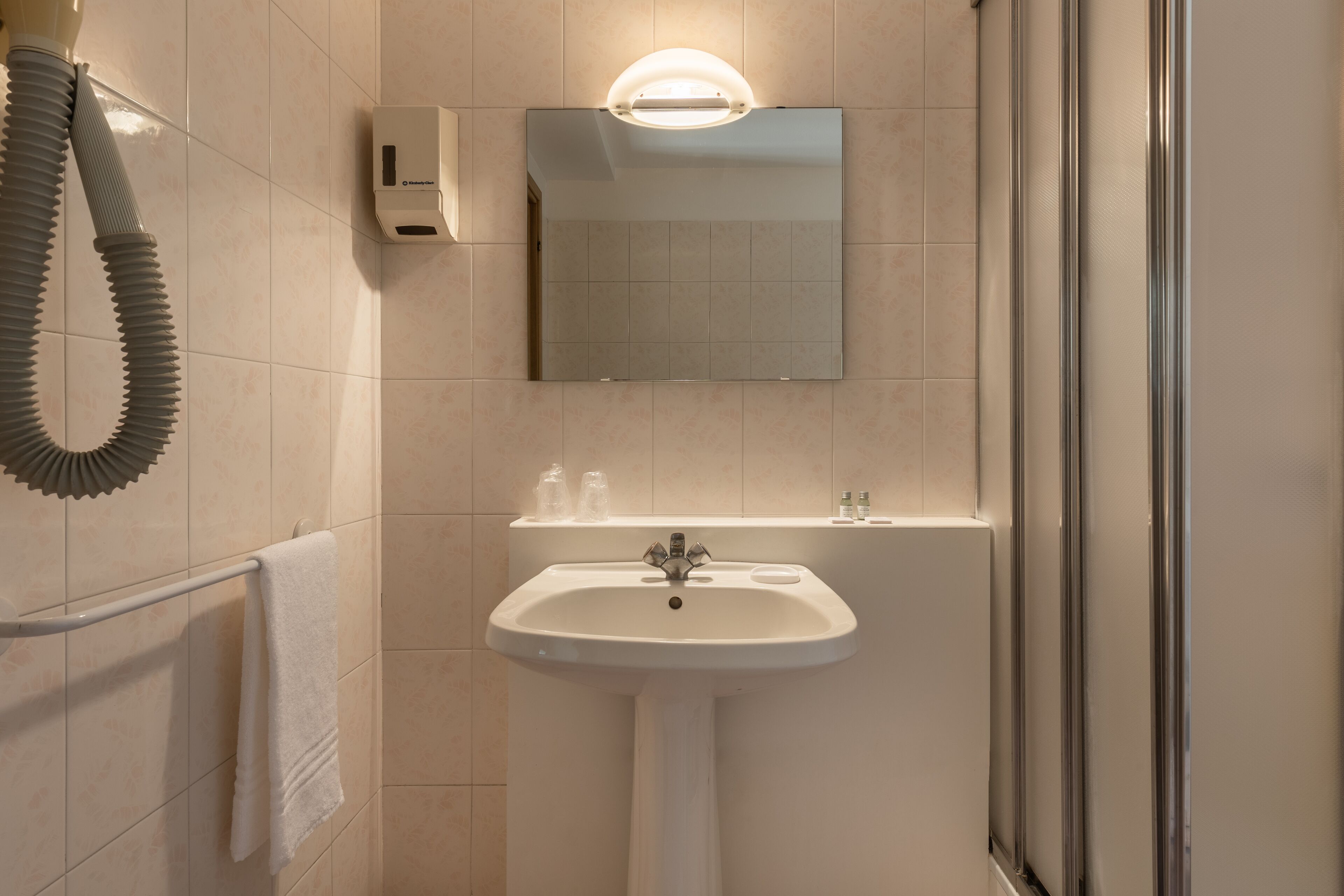 A bathroom with a white sink, a mirror, a hand dryer, and a towel rack.