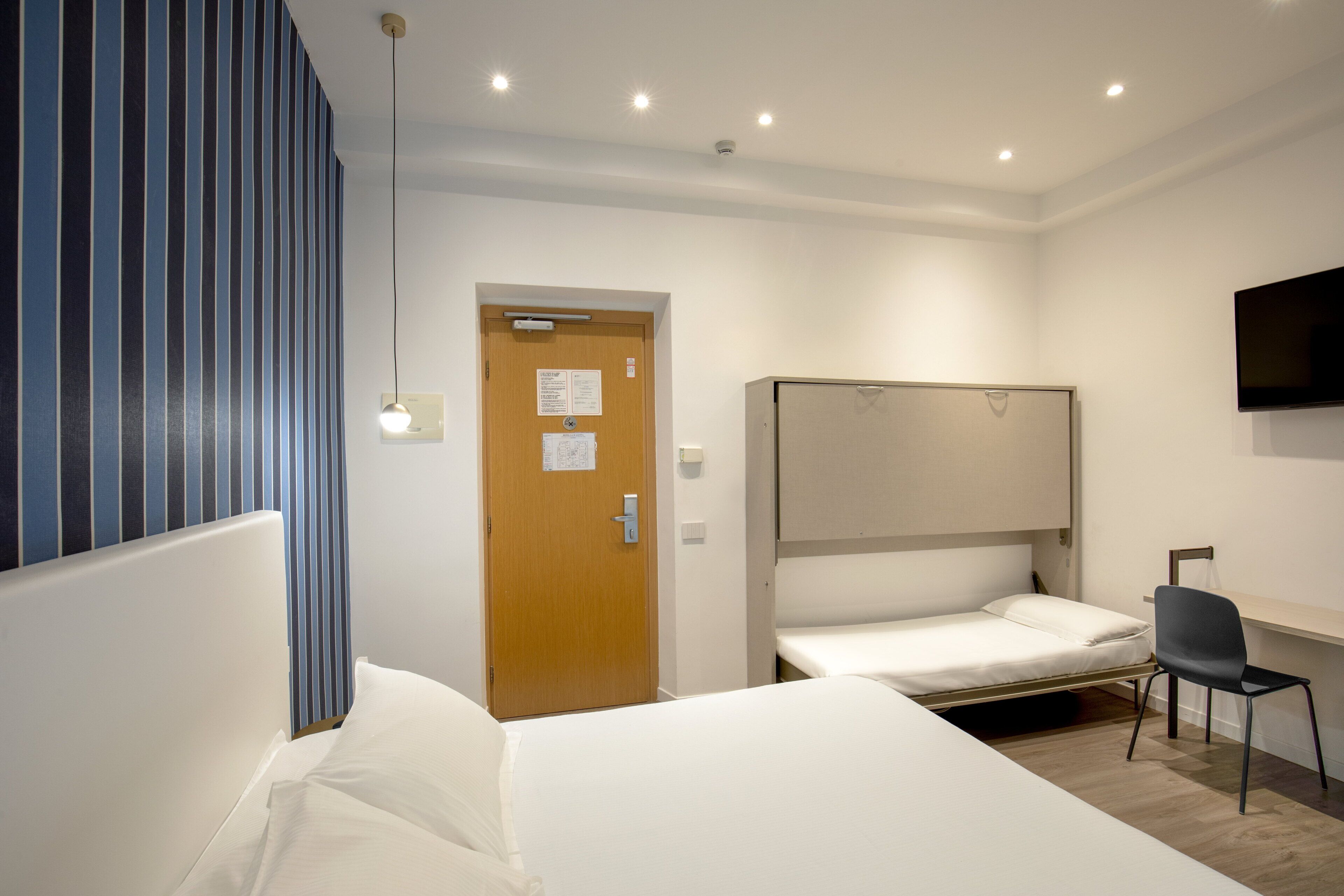 Une chambre d’hôtel avec deux lits simples, un bureau, une chaise, une télévision et une porte sur laquelle est affiché un avis.