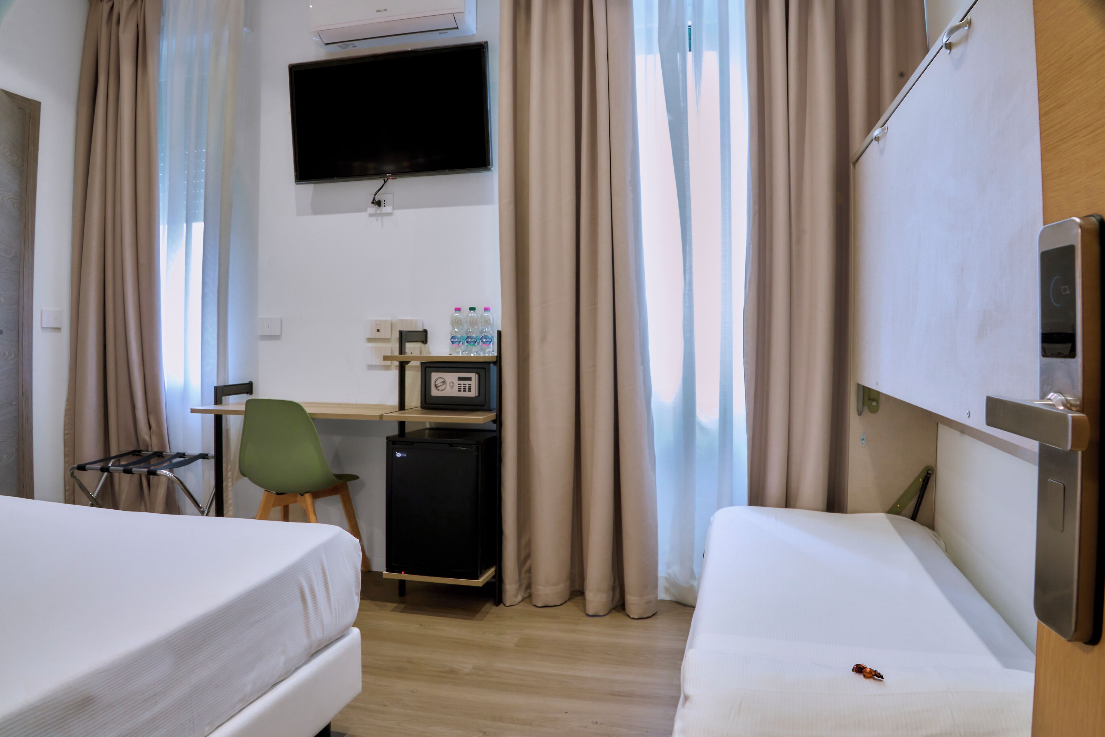 Hotellihuone, jossa on kaksi sänkyä, työpöytä tietokoneella, televisio ja minibaari.