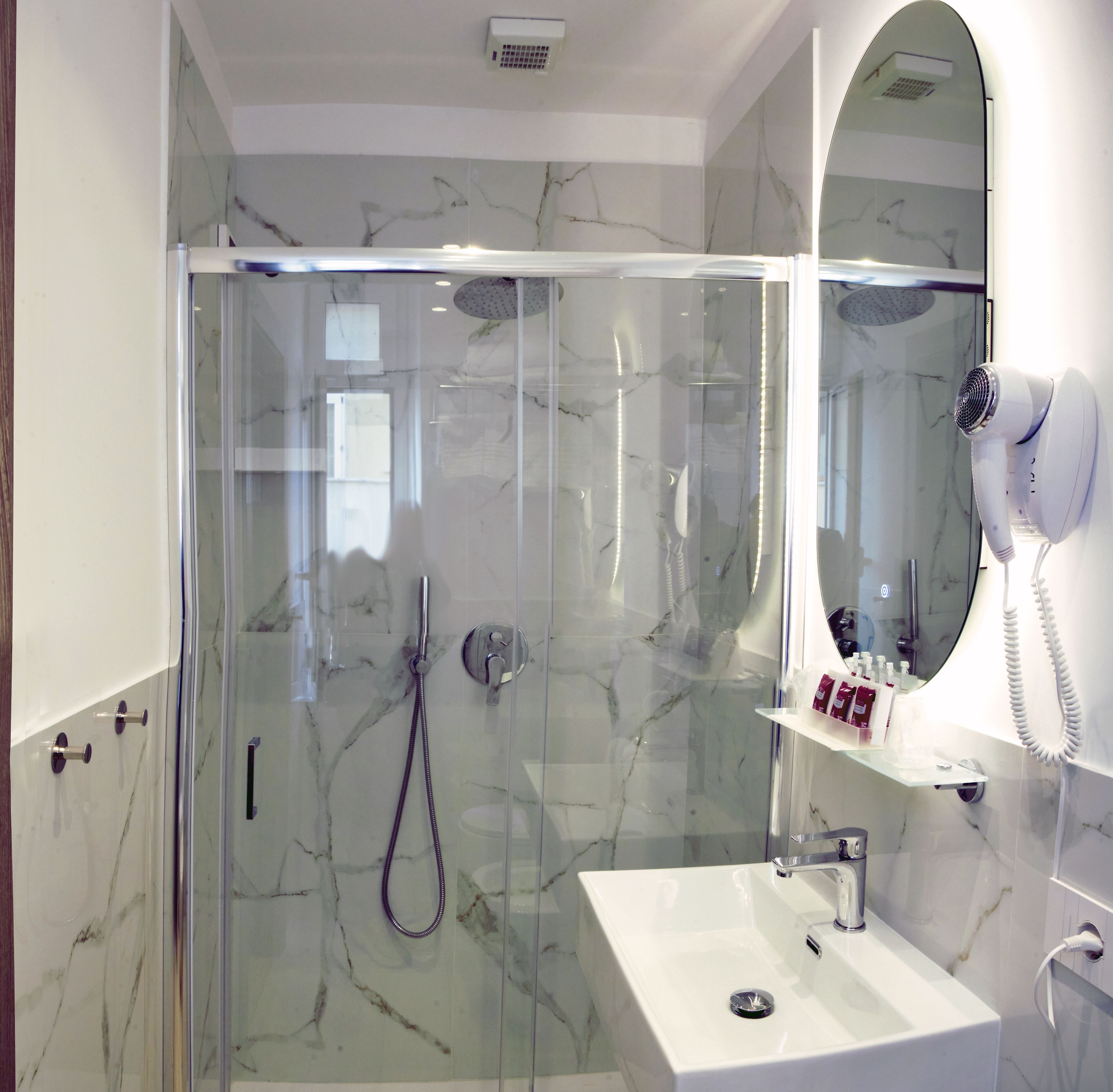 A modern bathroom with a glass-enclosed shower, a white sink, and a hairdryer mounted on the wall.