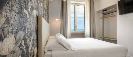 Un hotel moderno con una cama grande, vistas al mar a través de la ventana, un armario y un televisor de pantalla plana.