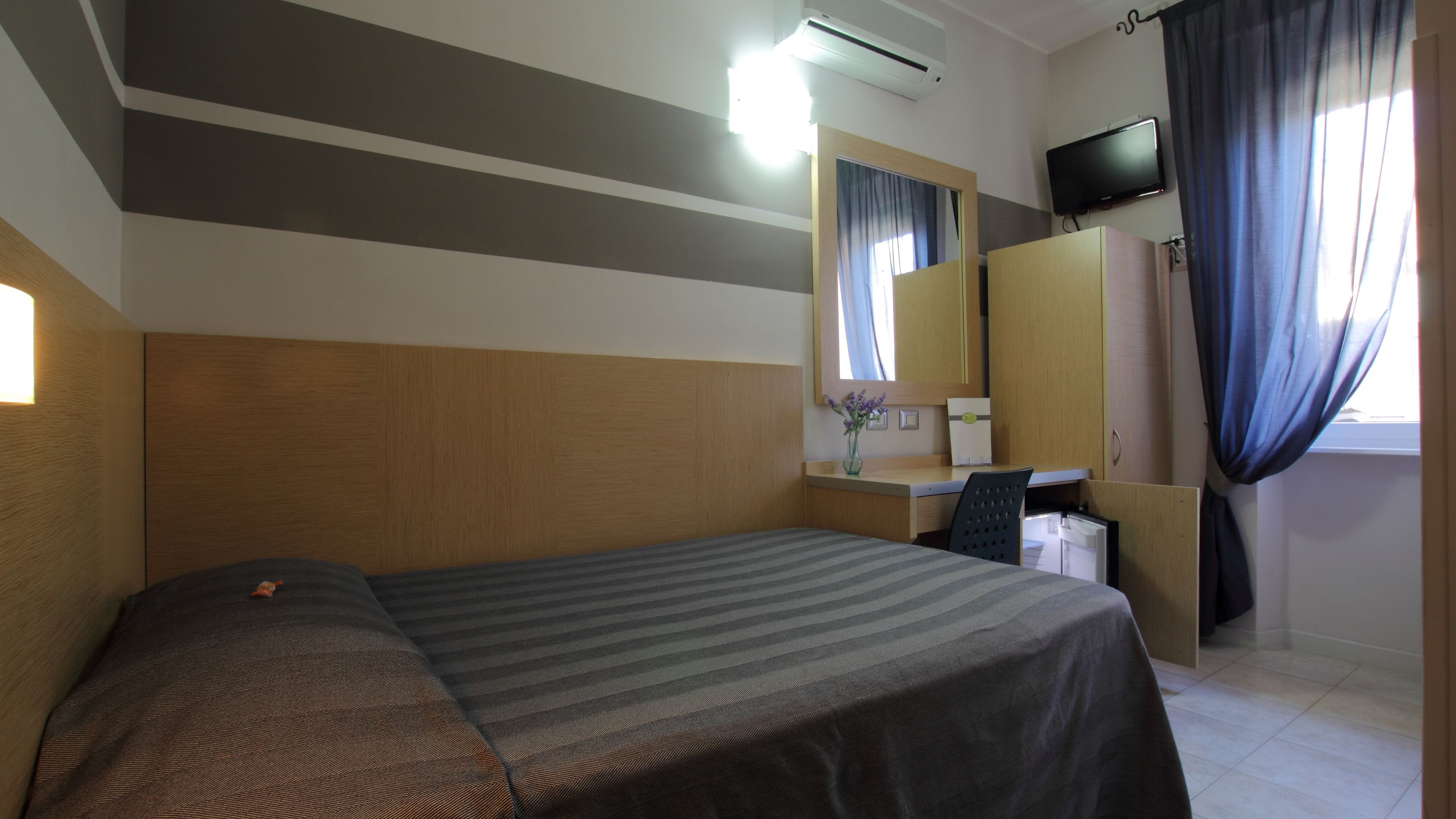 A hotel room with a bed, a desk, a chair, a TV, and a window with curtains.