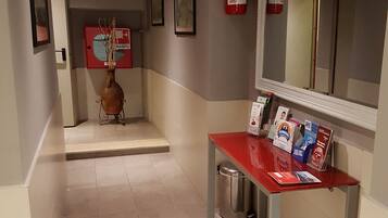 A hallway with a red reception desk, framed pictures on the walls, a fire extinguisher, and a trash bin.